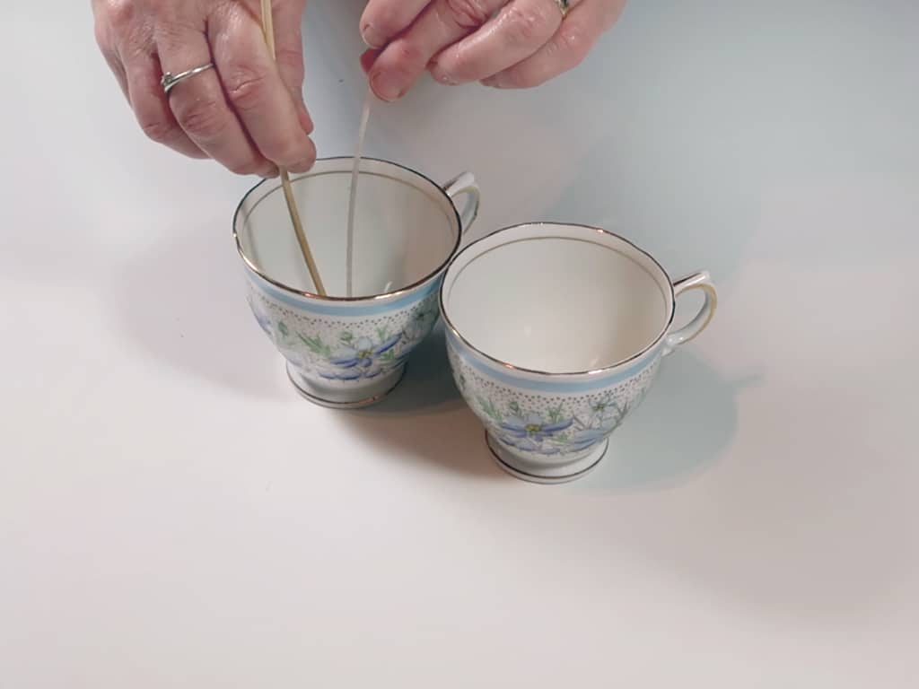 A woman wicks two teacups in prep for pouring candle wax