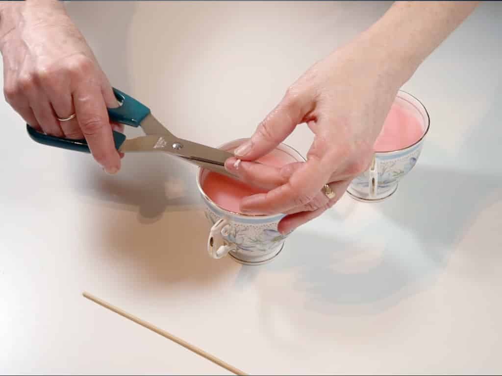 A woman trims the excess wick from a tea cup candle