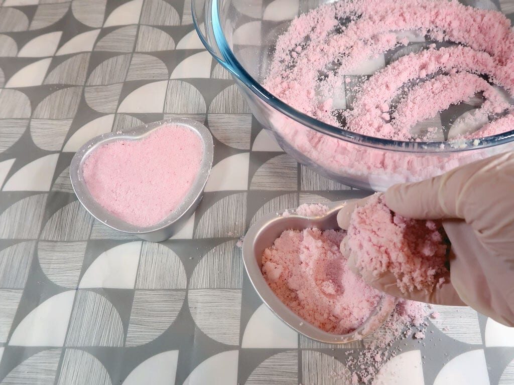 A woman fills a bath bomb mold with mixture