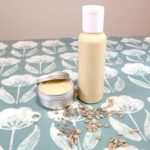 A bottle and pot of DIY eczema cream, surrounded by lavender buds and sunflower seeds
