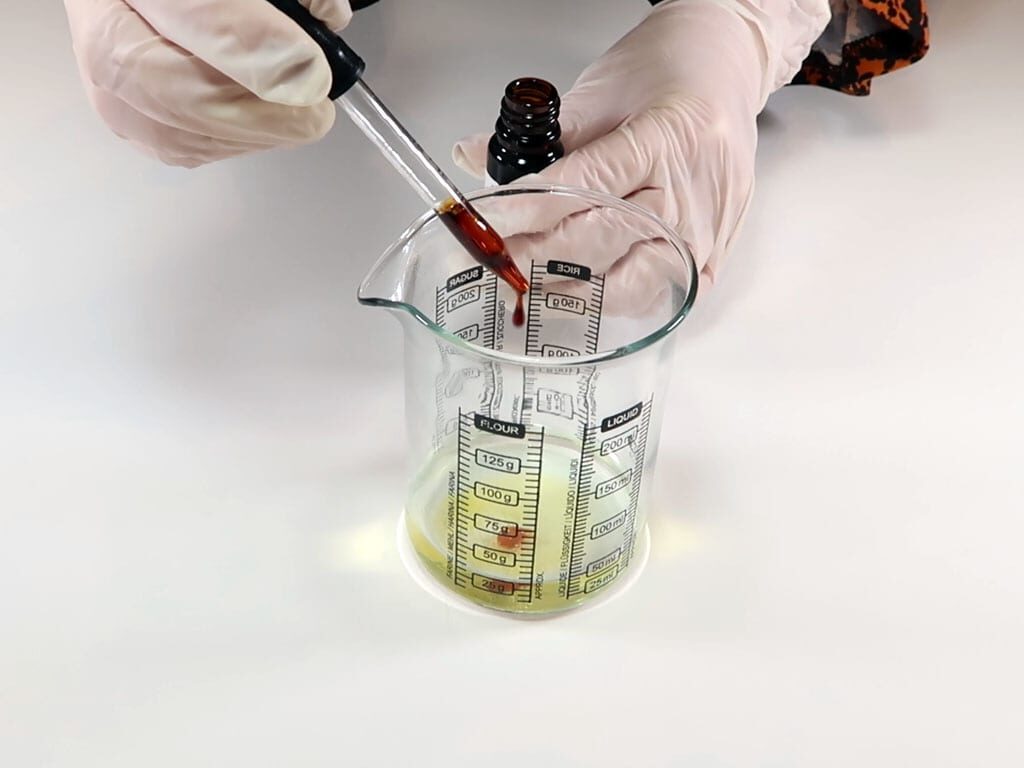 Essential oil is being added to the alcohol in a glass beaker