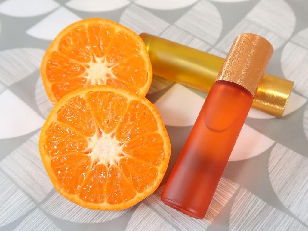 Two perfumes made with essential oils sat next to an orange