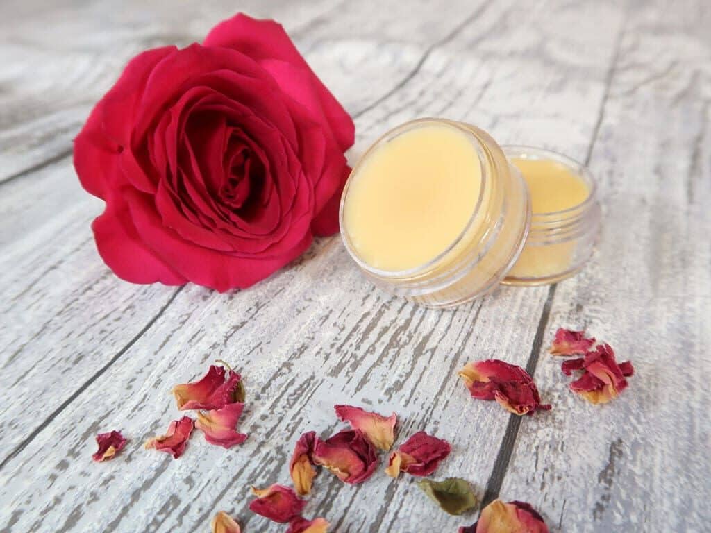 Two pots of homemade solid perfume with a rose and some rose petals around it