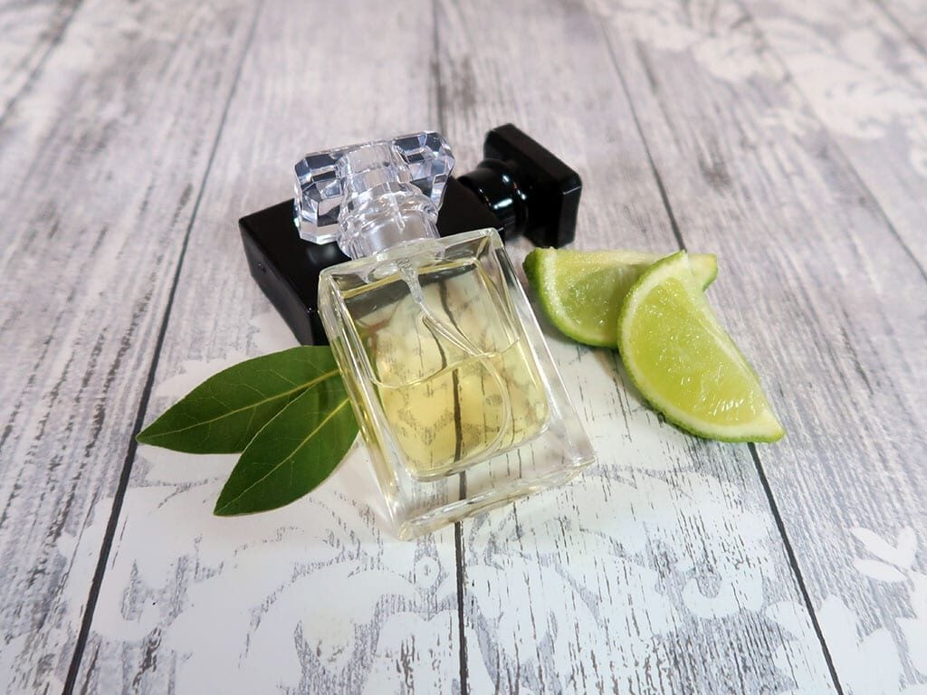 A 30ml bottle of cologne, sat next to another bottle, some lime segments and a couple of bay leaves