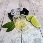 A 30ml bottle of cologne, sat next to another bottle, some lime segments and a couple of bay leaves