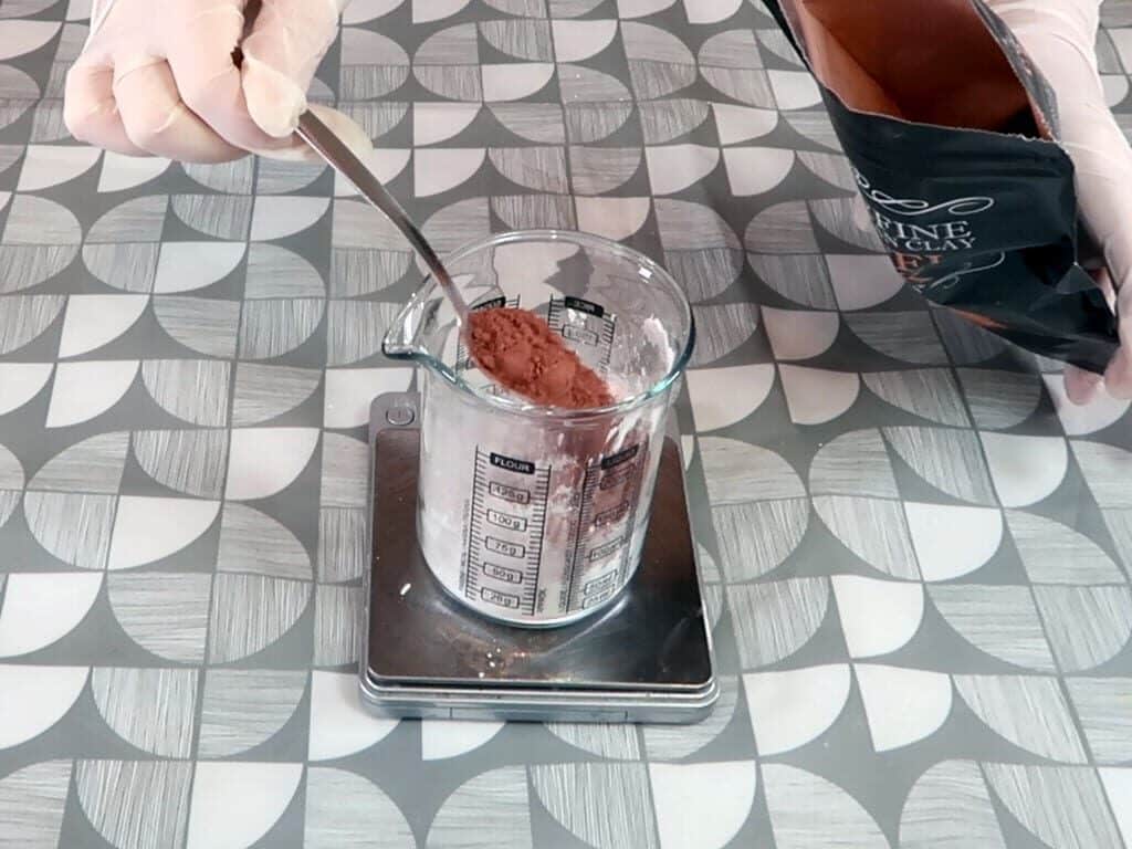 Pink clay being added to a beaker full of powdered ingredients