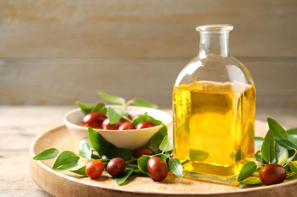 Glass bottle with jojoba oil and seeds on wooden table
