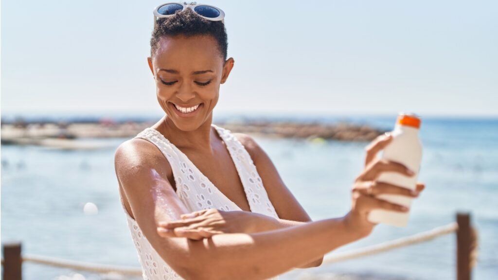 African american woman smiling confident applying sunscreen lotion at seaside