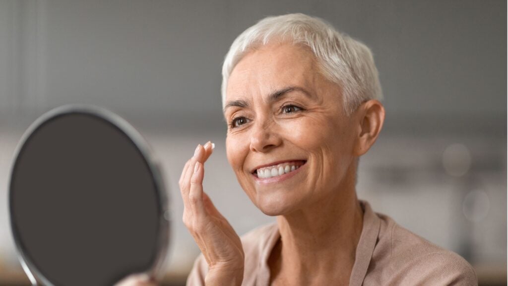 Cheerful Senior Lady Applying Facial Moisturizer Preventing Wrinkles