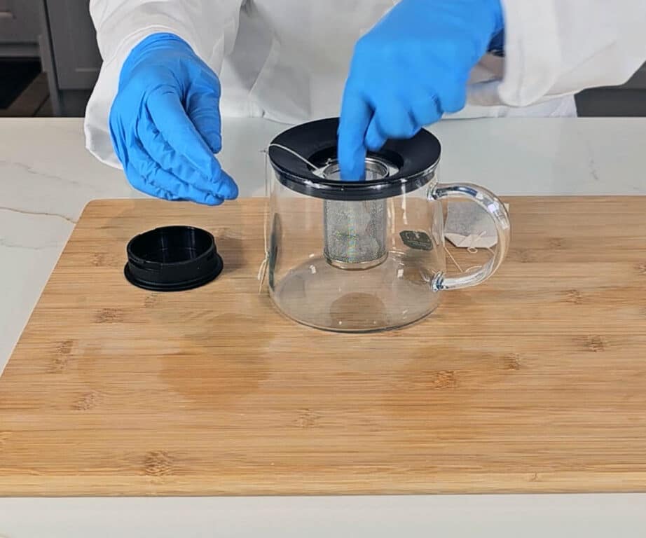 Green tea bags are placed into the infusion chamber of a glass tea pot.