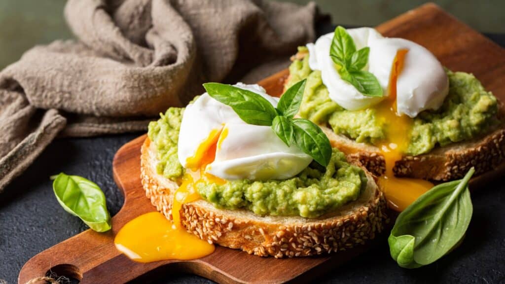 Smashed avocado sandwich with boiled poached egg with flowing yolk