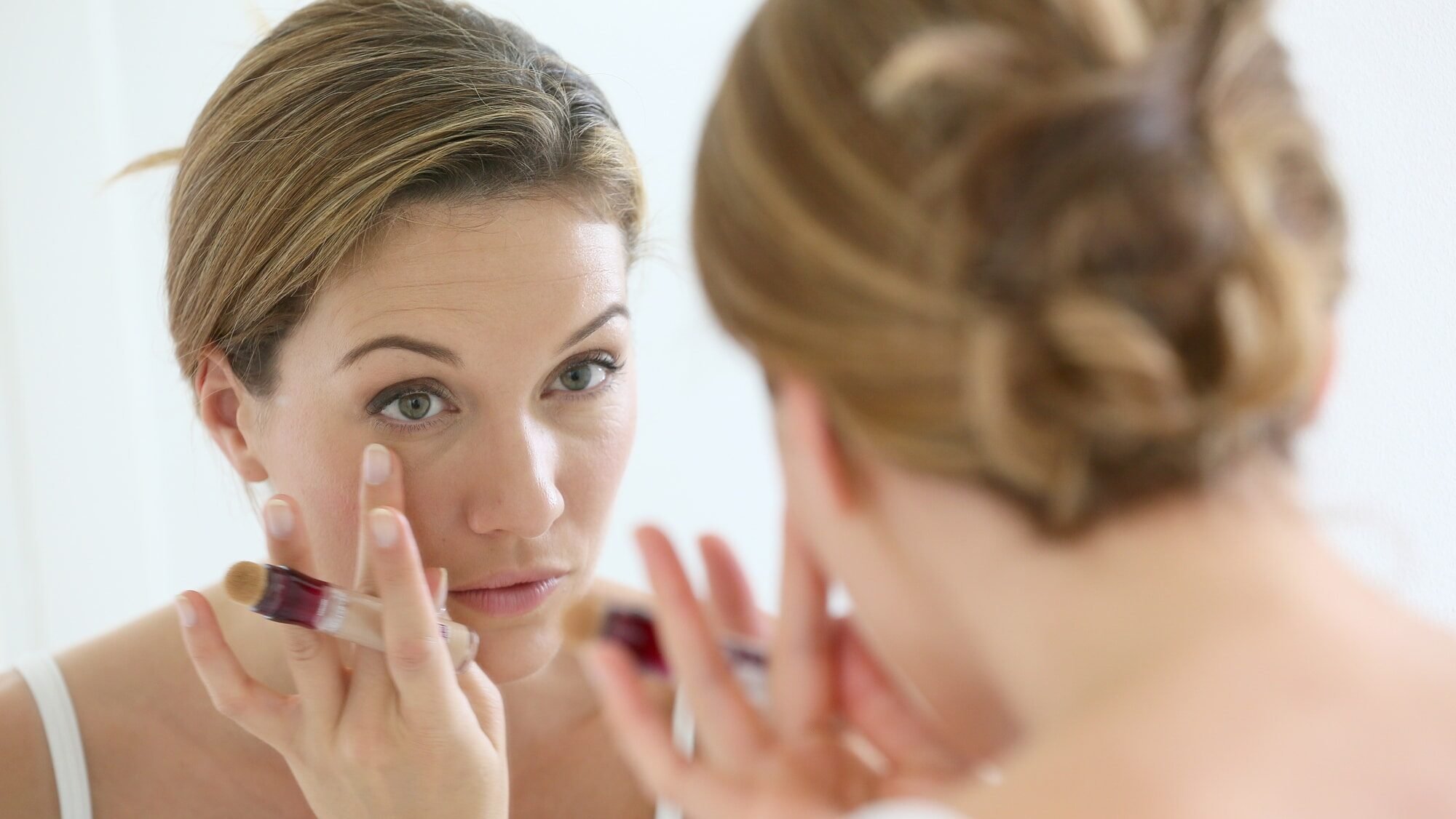 Beautiful blond woman applying concealer around eyes