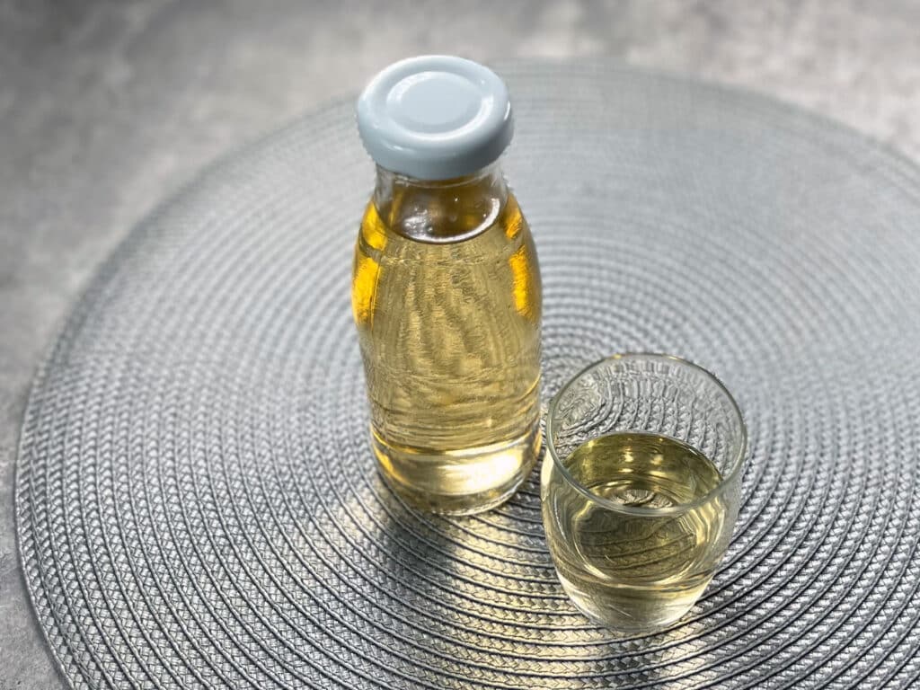 A bottle of apple cider vinegar hair rinse sits next to a glass of the same liquid