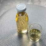A bottle of apple cider vinegar hair rinse sits next to a glass of the same liquid
