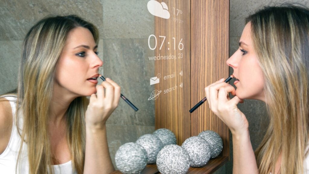 young woman applying lip liner in front of a smart mirror