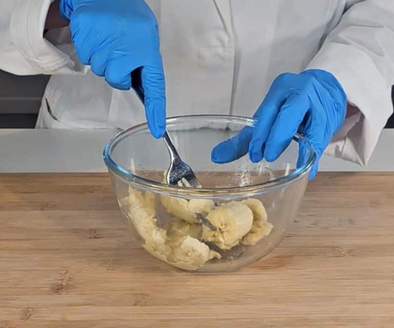 A banana is mashed with a fork in a mixing bowl