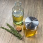 How to make rosemary oil: a bottle and mason jar of rosemary oil sit together next to spigs of fresh rosemary