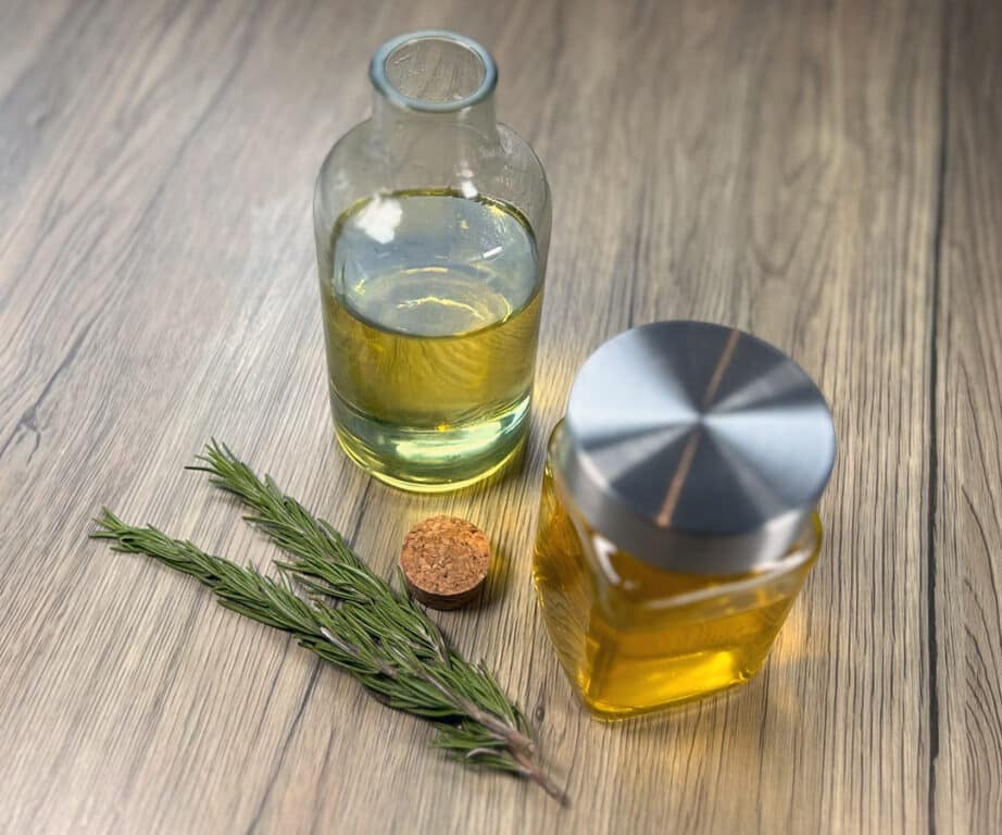 How to make rosemary oil: a bottle and mason jar of rosemary oil sit together next to spigs of fresh rosemary