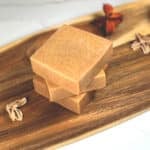 Three bars of natural homemade turmeric soap sit on a wooden board