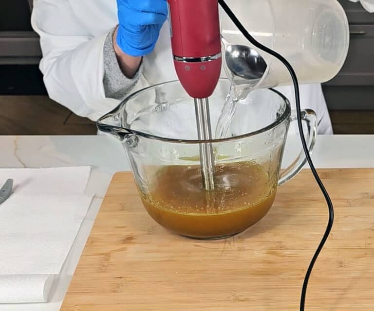 Liquid lye solution is poured into a mixture of oils and turmeric to make an emulsified soap batter