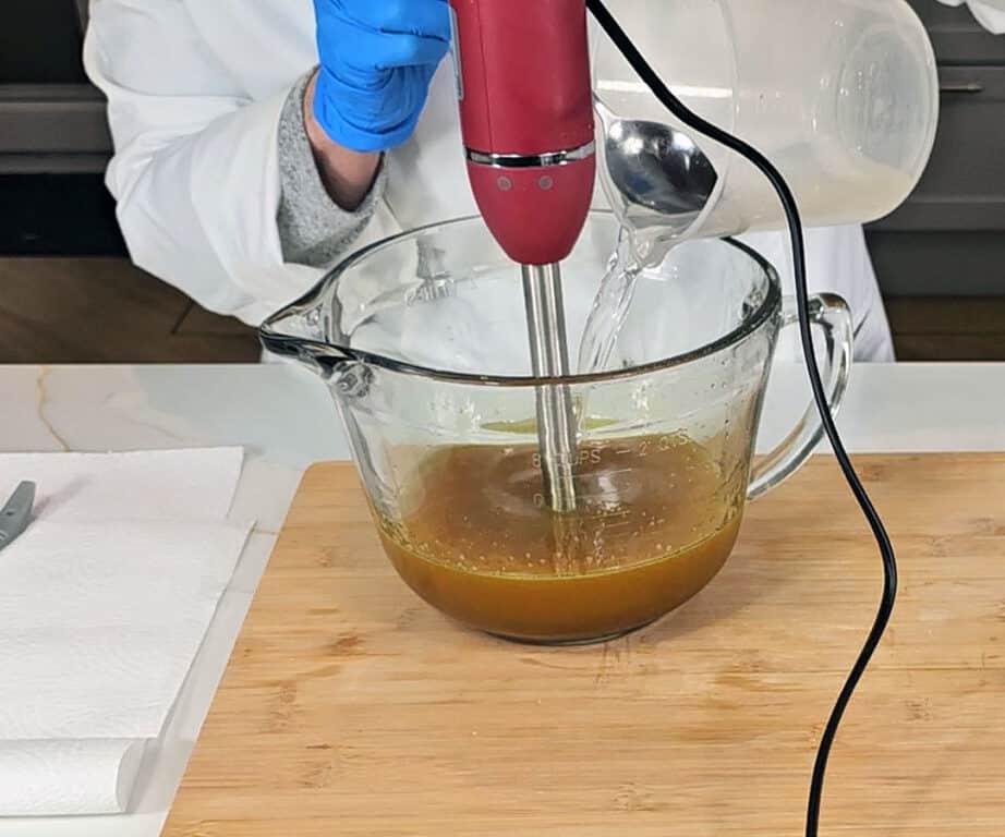 Liquid lye solution is poured into a mixture of oils and turmeric to make an emulsified soap batter