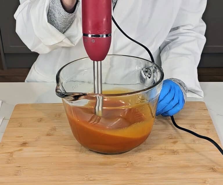The soap batter has emulsified and is being blended with a basic stick blender.