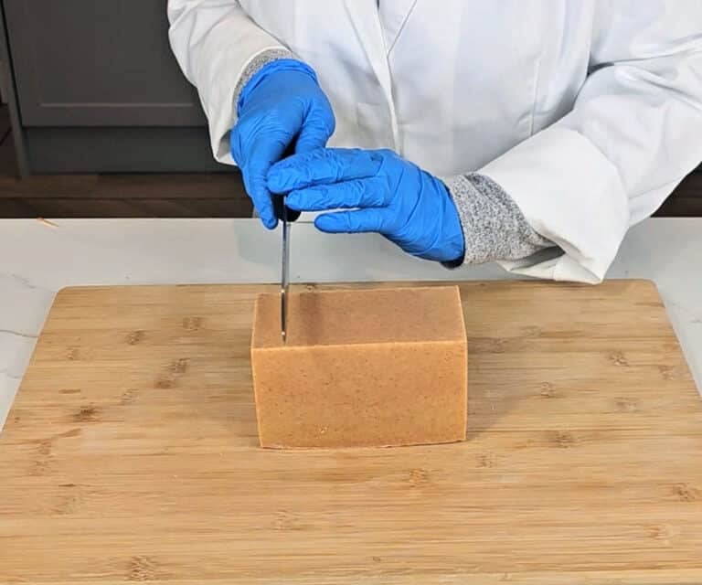 A loaf of turmeric soap is cut using a kitchen knife