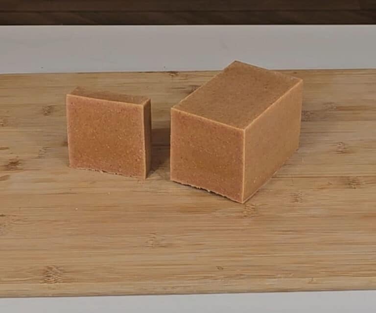 A bar of turmeric soap sits next to a loaf of the same soap.