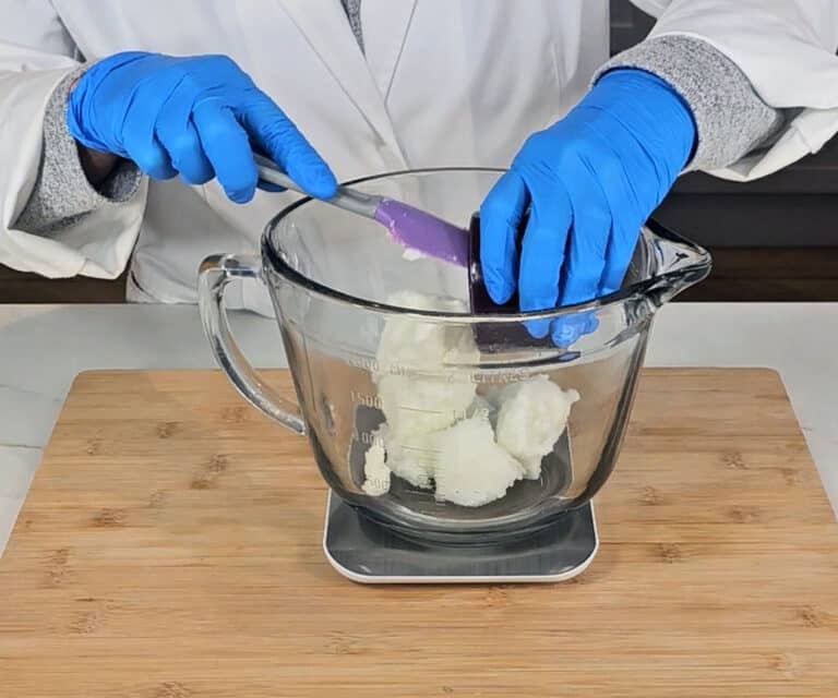 Shea butter is measured into a glass mixing bowl alongside coconut oil