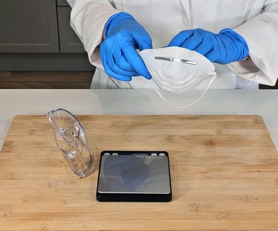 A protective mask is being applied, and a pair of goggles sits next to a set of digital weighing scales