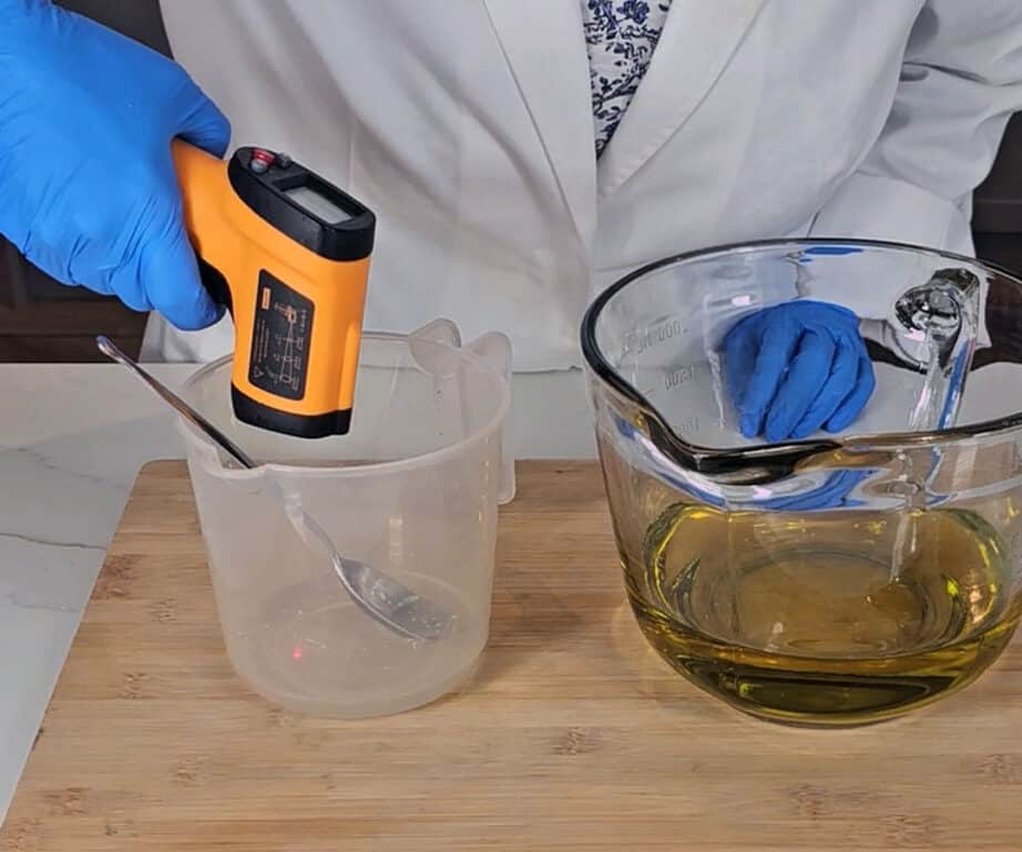 The lye solution is being measured with a lazer thermometer while it sits next to the mixing bowl of olive oil