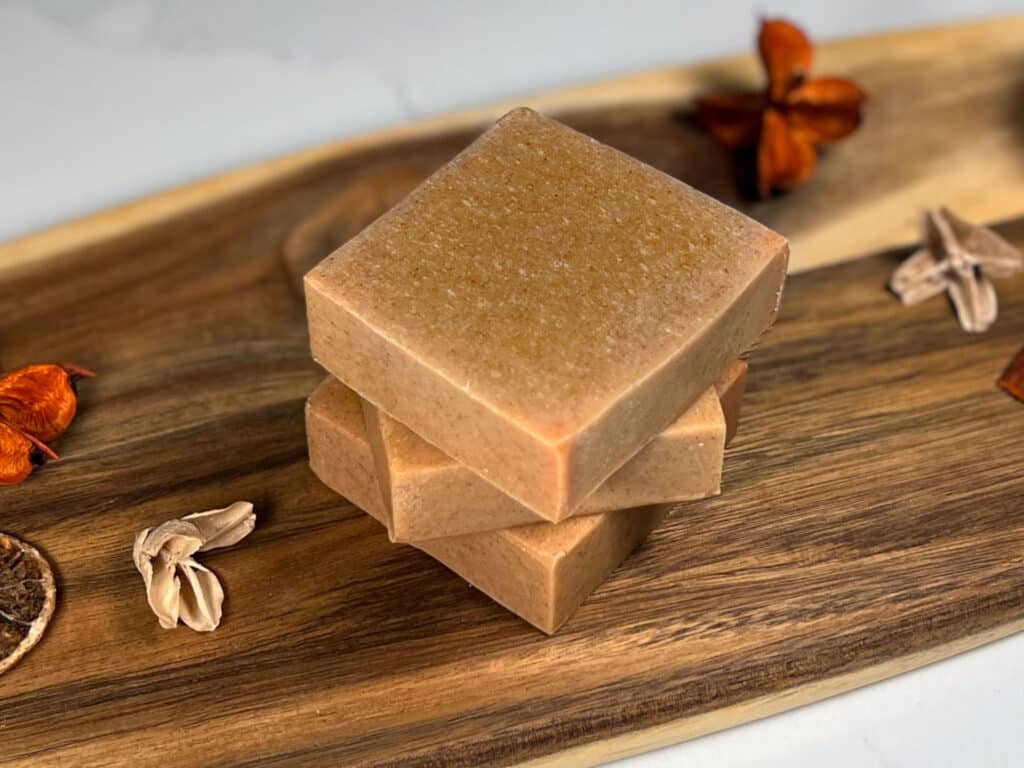 Three bars of natural homemade turmeric soap sit on a wooden board
