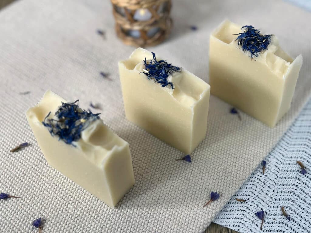 Three bars of DIY lavender soap, topped with purple flowers, sit together in a row.