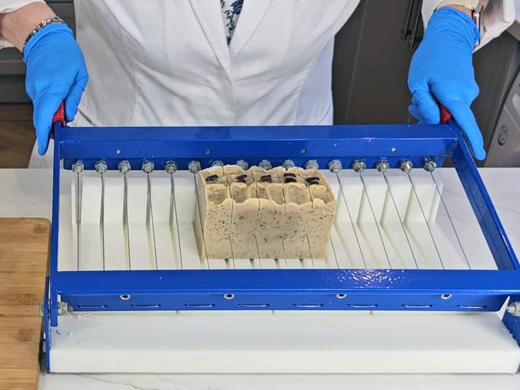 The loaf of soap is cut into bars using a soap cutter
