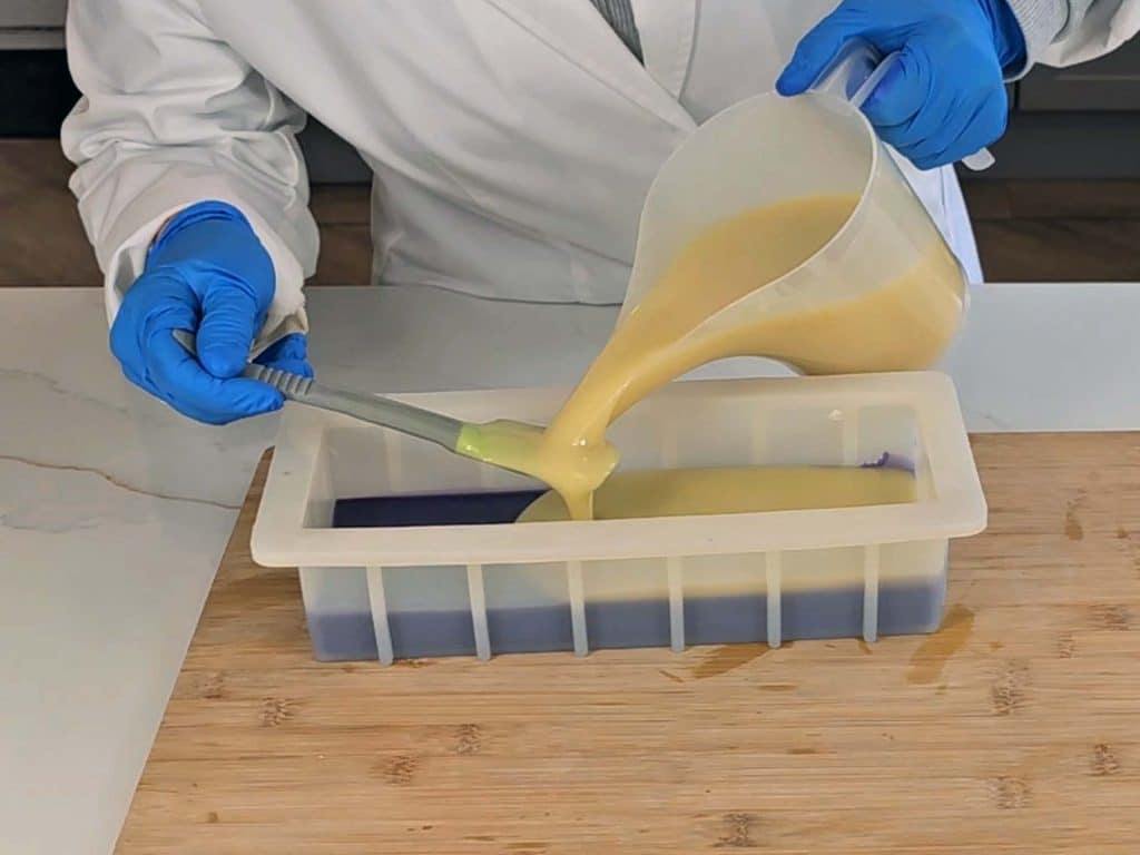 The undyed soap batter is layered ontop of the surple soap batter in the mold