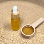 DIY cuticle oil sits next to a spoon with some of the oil in it