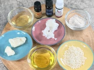 Lotion ingredients on plates and in bowls sit together on a wooden base