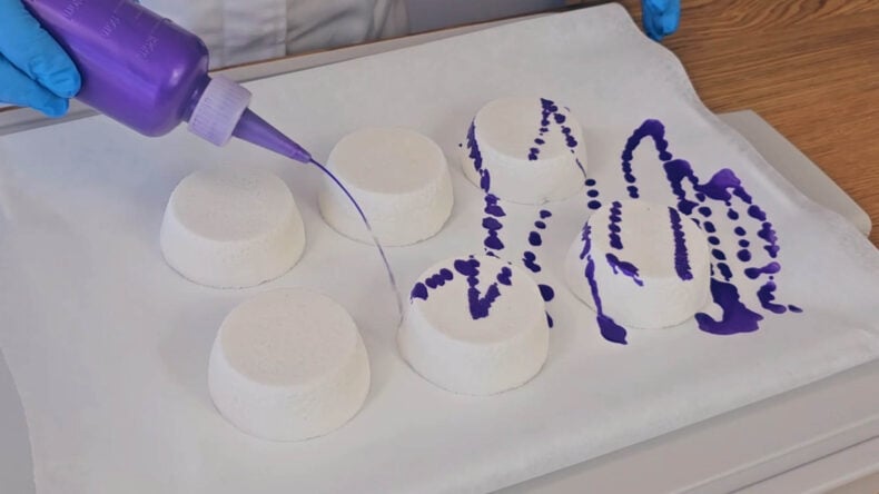 Drizzling purple mica mixture over homemade shower steamers in a zigzag pattern Drizzling purple mica mixture over homemade shower steamers in a zigzag pattern